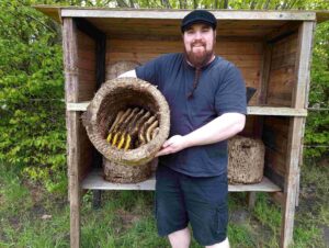 Fabian Kalis präsentiert eine traditionelle Korbbeute mit frei gebauten Bienenwaben der wesensgemäßen Bienenhaltung.
