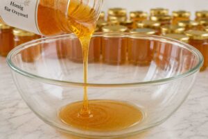 Honig fließt aus einem Glas in eine große Glasschüssel zur Herstellung von Oxymel.