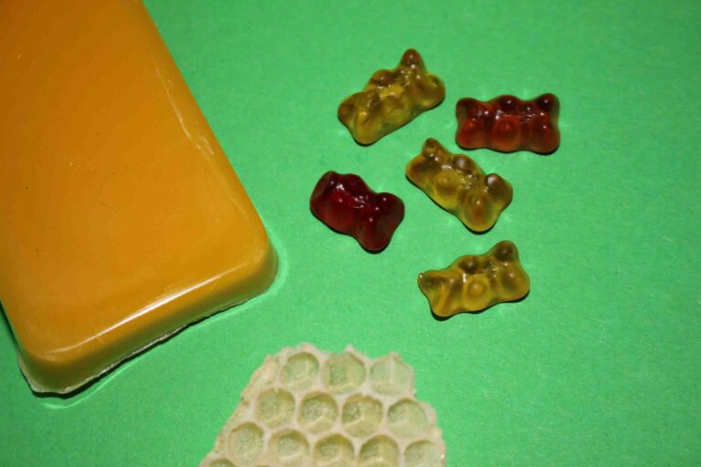 Block aus Bienenwachs, ein Stück Bienenwabe und Gummibärchen aus Bienenwachs auf grünem Hintergrund.